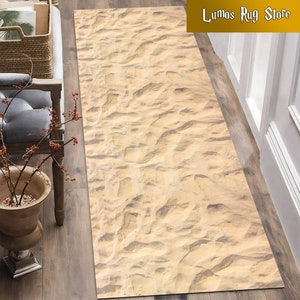 May include: A beige and brown rectangular rug with a sand-like texture. The rug has a subtle pattern of footprints.