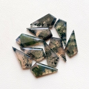 Puede incluir: Una colección de diez cabujones de ágata musgosa verde y gris, cada uno cortado en forma de punta facetada. Las piedras tienen una apariencia translúcida con una variedad de patrones verdes y grises.