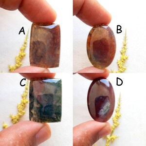 Puede incluir: Cuatro piedras preciosas pulidas de varias formas y colores. Las piedras preciosas están sostenidas por los dedos de una persona. Las piedras preciosas incluyen una piedra rectangular marrón, una piedra ovalada marrón, una piedra rectangular verde y una piedra ovalada rojo oscuro.