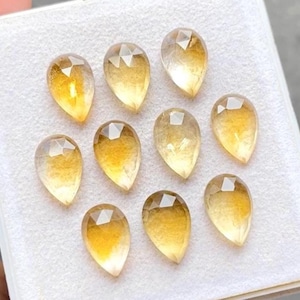 May include: Ten faceted, teardrop-shaped gemstones are displayed. The gems have a colour gradient, going from clear at the top to a rich, golden-yellow at the base. Each stone is cut with multiple facets, creating a sparkling effect.