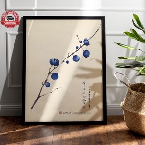 Puede incluir: Una impresión enmarcada de una pintura de acuarela de una rama con bayas azules y caligrafía japonesa. La impresión está sobre un fondo crema y tiene un marco negro.