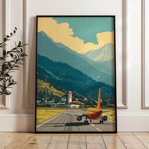May include: A framed art print depicts an orange airplane on a runway, with a mountain range in the background. The sky is a gradient of yellow and blue. A second plane flies in the distance. The artwork has a vintage travel poster style.