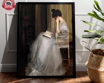 Può includere: Stampa artistica incorniciata di una donna che legge un libro, seduta su una sedia. L'opera presenta una donna in un lungo abito bianco fluente, con uno sfondo scuro e un tocco d'oro. La stampa è in una cornice nera.