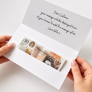 K&ouml;nnte beinhalten: Eine wei&szlig;e Gru&szlig;karte mit einem Einsteckfach, das einen Zehn-Pfund-Schein der Bank of England enth&auml;lt. Die Karte ist mit folgendem schwarzen Text bedruckt: Dear Customer, your message will be displayed here if you choose to add the message option. Love Katie x.