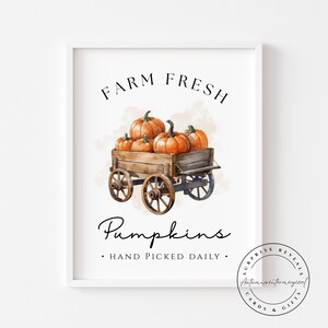 May include: A framed print with a watercolour illustration of a wooden cart laden with orange pumpkins. The text "FARM FRESH" and "Pumpkins" are above and below the cart, with "HAND PICKED DAILY" below. A circular logo is in the bottom right corner.