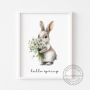 May include: A framed watercolour print featuring a grey rabbit clutching a bunch of white daisies. The words "hello spring" are written below. The print is in a white frame.