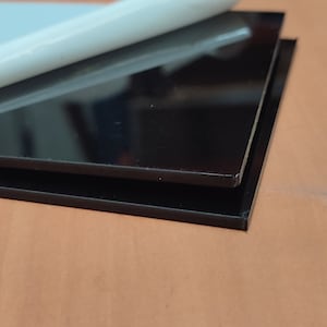 Peut inclure: Deux feuilles de plastique acrylique noir, l'une partiellement décollée pour révéler un film protecteur.