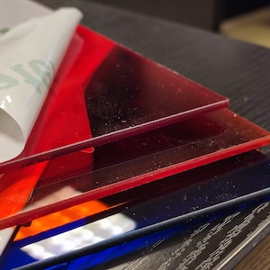 Op de afbeelding: Stapel van vier acrylaatplaten in rood, oranje en blauw. De platen zijn doorschijnend en hebben een lichte glans.