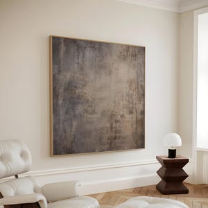 Puede incluir: Una escena de salón moderno con una gran pintura abstracta en un marco de madera. Un sillón y un otomán de cuero blanco sobre un suelo de parquet. Una pequeña mesa auxiliar de madera sostiene una lámpara blanca. El texto "CURIOSITY ES ART | PRINTABLE WALL ART" es visible.
