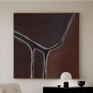 Puede incluir: Gran pintura abstracta enmarcada con un fondo marrón oscuro y un diseño lineal en blanco y negro. La obra de arte cuelga sobre un mueble negro. Una silla y un otomán blancos están en primer plano.