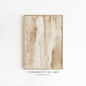 Puede incluir: Una impresión enmarcada de arte mural con una paleta de colores neutros. La obra presenta pinceladas verticales en tonos beige y crema, creando un efecto texturizado. El marco es de color marrón claro. El texto "CURIOSITY ES ART PRINTABLE WALL ART" está en la parte inferior.