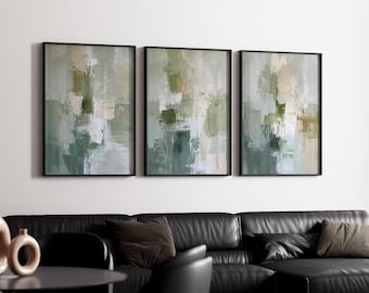 May include: Three abstract paintings in black frames with green, white, and beige brushstrokes. The paintings are hung on a white wall above a black leather sofa.