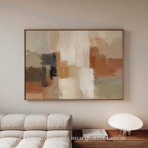 May include: Abstract canvas print with a neutral colour palette. The artwork features rectangular shapes in beige, brown, grey, and white. The canvas is framed in a thin, light brown wooden frame. The text "CURIOSITY ES ART | HIGH QUALITY CANVAS" is visible at the bottom.