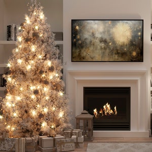 May include: A white flocked Christmas tree with gold ornaments and white lights, decorated with presents underneath. A fireplace with a roaring fire is in the background, and a framed abstract painting hangs above the fireplace.