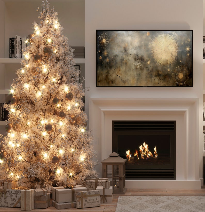 May include: A white flocked Christmas tree with gold ornaments and white lights, decorated with presents underneath. A fireplace with a roaring fire is in the background, and a framed abstract painting hangs above the fireplace.