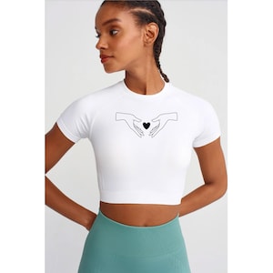 May include: White crop top with short sleeves featuring a black line drawing of two hands holding a heart in the center.