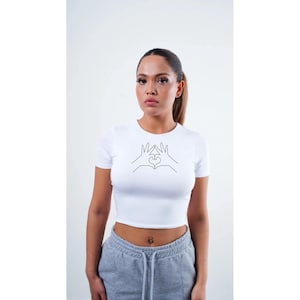 May include: White crop top with a black line drawing of two hands making a heart shape.