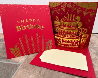 May include: Red and gold pop-up birthday card with a cake and candles. The card has a blank space for a message. "Happy Birthday" is written on the card.