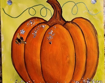 Peut inclure: Peinture d'une citrouille orange avec une tige marron, une abeille et des éléments décoratifs. Le fond est jaune avec des volutes vertes et des embellissements scintillants. La base de la citrouille est décorée de morceaux bleus et argentés.