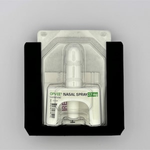 May include: A white nasal spray bottle with a clear plastic cap, labeled "OPVEE&reg; NASAL SPRAY 2.7 mg (intranasal)". The bottle is packaged in a black plastic holder.