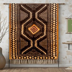 May include: A rectangular, brown and gold patterned rug with a central diamond design and fringe. The rug is displayed on a metal stand against a textured wall. A framed sign reads "MOROCCO GRAPHIC DESIGN".