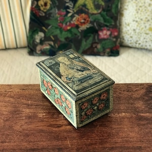 Könnte beinhalten: Eine Vintage-Blechdose mit floralem Design und einem Bild einer Frau auf dem Deckel. Der Text auf dem Deckel lautet "Virtue is Reward of itself, and Vice its own Punishment."