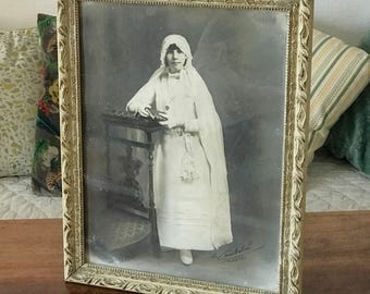 Grande fotografia in bianco e nero di un giovane comunicante in una cornice di legno dipinta di bianco. Circa 1920.