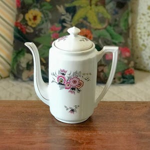 Witte porseleinen theepot en koffiezetapparaat met grijze en roze decoratie en gestileerde bloemen