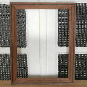 Puede incluir: Un marco de fotos rectangular de madera con acabado marrón y líneas negras de acento. El marco tiene un diseño simple y clásico, adecuado para exhibir fotografías u obras de arte. El fondo presenta paneles blancos y negros texturizados.