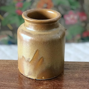 Peut inclure: Petit pot en céramique fait à la main, avec un corps arrondi et un col étroit. Le pot présente un glaçage brun terreux moucheté avec des stries plus claires et une surface subtilement texturée. Il s'agit probablement d'une pièce décorative ou fonctionnelle.