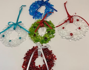May include: A collection of colorful, small, glass bead wreaths with ribbon hangers. The wreaths are in shades of blue, green, red, and white. Each wreath is adorned with a matching ribbon bow. These ornaments are perfect for holiday decorating.