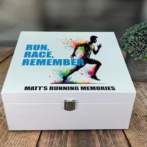 May include: A white wooden box with a hinged lid and metal clasp. The lid displays a colourful graphic of a runner, with the text "RUN, RACE, REMEMBER" and "MATT'S RUNNING MEMORIES" in blue and black.