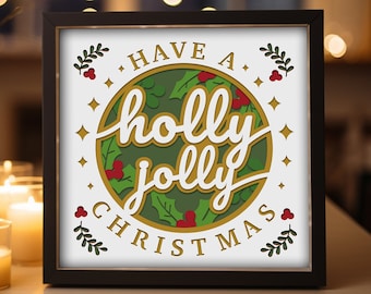 May include: A framed Christmas artwork with the message "Have a holly jolly Christmas." The design includes a green holly wreath with red berries and gold detailing on a white backdrop. The frame is black.
