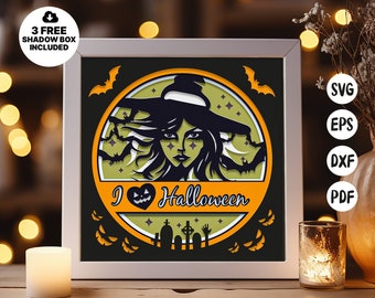 May include: A framed Halloween-themed paper cut art piece. The artwork features a witch with bats, a graveyard, and the text "I love Halloween." The piece is in a white frame and includes the text "3 FREE SHADOW BOX INCLUDED."