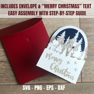 May include: A red envelope next to a white Christmas card with a cut-out winter scene and gold text that reads "Merry Christmas". The card includes a step-by-step guide and the text "SVG - PNG - EPS - DXF".