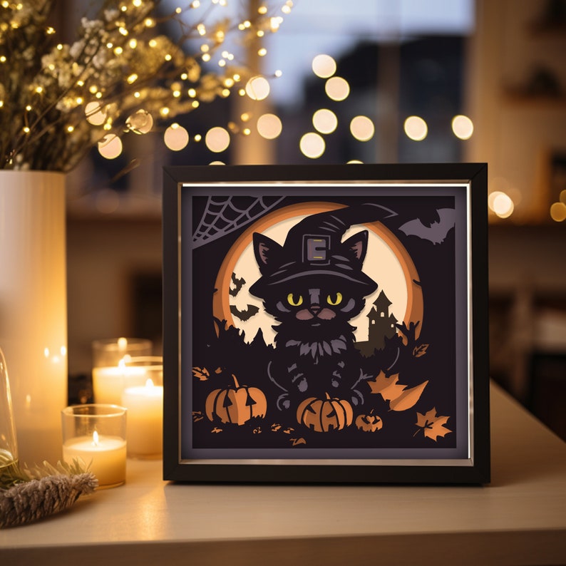 May include: A framed Halloween-themed art piece featuring a black cat wearing a witch hat, set against a full moon. The artwork includes pumpkins, bats, and a spooky silhouette of a haunted house, all in shades of black, orange, and tan.