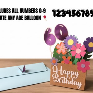 May include: A birthday card with a floral arrangement and the number 60. The card says "Happy Birthday" and includes the numbers 0-9 to create any age balloon. A light blue envelope with a butterfly is also included.