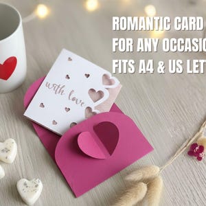 Pu&ograve; includere: Una tazza bianca con un cuore rosso, un biglietto rosa con ritagli a forma di cuore e una busta abbinata. Il biglietto recita "with love" e viene visualizzato il testo "ROMANTIC CARD FOR ANY OCCASION FITS A4 & US LETTER".