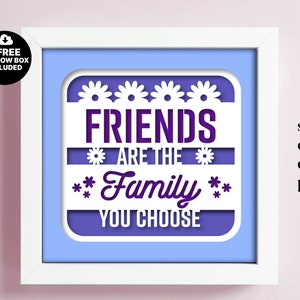 May include: White frame with a light blue background and a white cutout design. The design features the text "FRIENDS ARE THE FAMILY YOU CHOOSE" with flowers surrounding the text. The text is in purple.