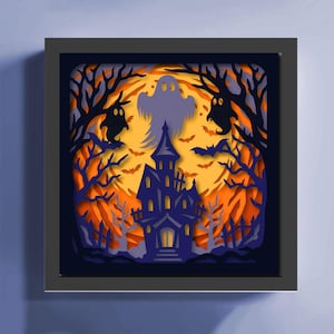 May include: A framed Halloween-themed paper art piece. The artwork features a haunted house, bats, ghosts, and trees in shades of orange, purple, and black. The background is a gradient of orange and yellow, creating a spooky atmosphere.