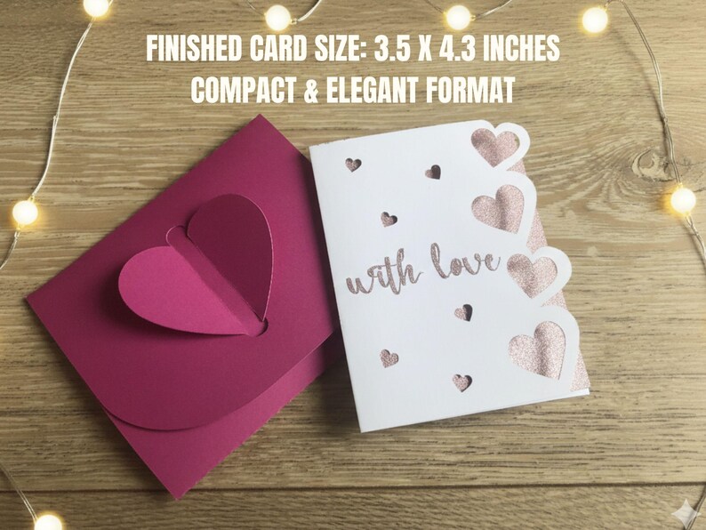 Pu&ograve; includere: Un biglietto magenta con un cuore a comparsa e un biglietto bianco con ritagli a forma di cuore e la scritta "with love". Le dimensioni finali del biglietto sono 8,9 x 10,9 cm. I biglietti sono su una superficie di legno.