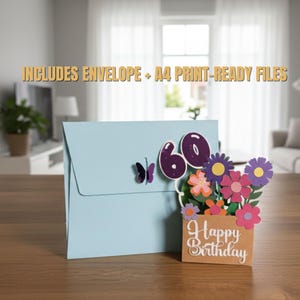 May include: A light blue birthday card with a butterfly and the number 60. The card features a pop-up bouquet of colorful paper flowers and a small sign that says "Happy Birthday". The text "INCLUDES ENVELOPE + A4 PRINT-READY FILES" is also visible.
