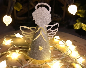 May include: A glittery silver angel Christmas ornament with a halo and wings. The angel is surrounded by a string of star-shaped lights and other small round lights, creating a festive holiday display.