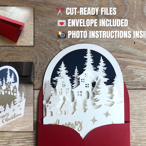 Può includere: Un biglietto di Natale rosso con un design bianco a strati raffigurante una scena di villaggio invernale con alberi e case. Il biglietto include il testo "Merry Christmas" e viene fornito con una busta. È visibile anche il testo "CUT-READY FILES", "ENVELOPE INCLUDED" e "PHOTO INSTRUCTIONS INSIDE".