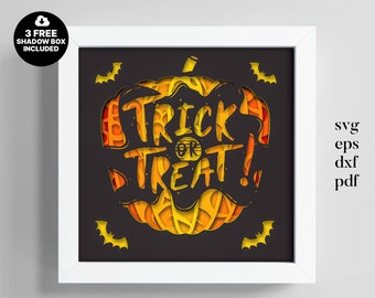 May include: A framed Halloween-themed paper cut art piece. The design features a pumpkin shape with the words "Trick or Treat" cut out in yellow and orange layers. Includes bat silhouettes and the text "3 FREE SHADOW BOX INCLUDED".