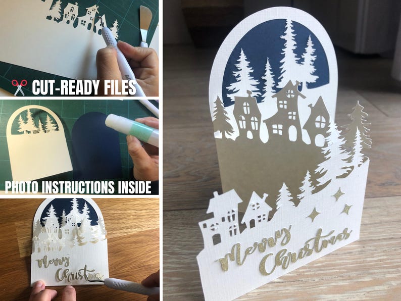 May include: A white paper Christmas card with a layered design featuring a village scene and pine trees. The card has the words "Merry Christmas" in gold script. The card is on a wooden surface.
