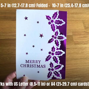 May include: A white Christmas card with a purple holly design and star cutouts. The card reads "MERRY CHRISTMAS" and measures 5x7 inches (12.7x17.8 cm) folded and 10x7 inches (25.4x17.8 cm) open. It is designed for US Letter or A4 cardstock.