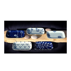 May include: Five small rectangular ceramic dishes with blue and white floral patterns. The dishes are arranged on a wooden surface with small grey stones.