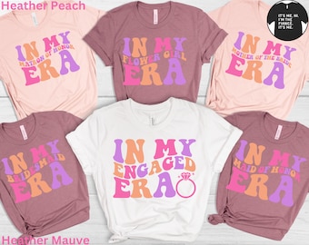 May include: Five t-shirts with different text designs in a retro font style. The shirts are in various colors, including pink, white, and mauve. The text on the shirts includes "In My Era" with different titles like "Matron of Honor", "Flower Girl", "Mother of the Bride", "Bridesmaid", and "Engaged".