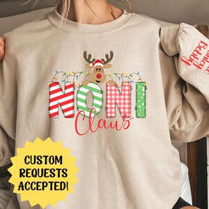 May include: Beige sweatshirt with a red, green, and white "Noni Claus" graphic featuring a cartoon reindeer with a red hat and lights. The text "Jake Ashley Happy" is on the sleeve.